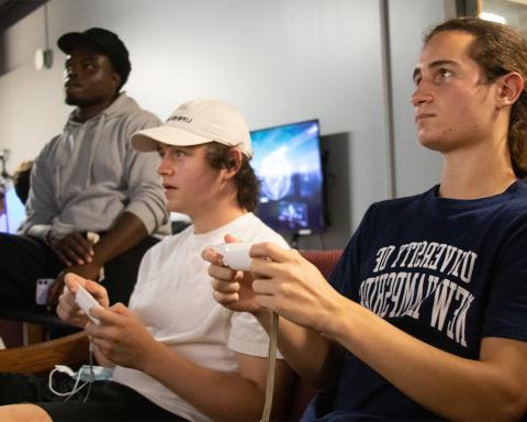 三个学生坐在沙发上玩电子游戏
